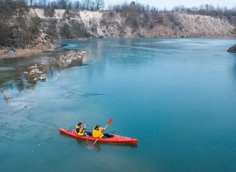 two athletic man floats on a red boat in calm blue waters river